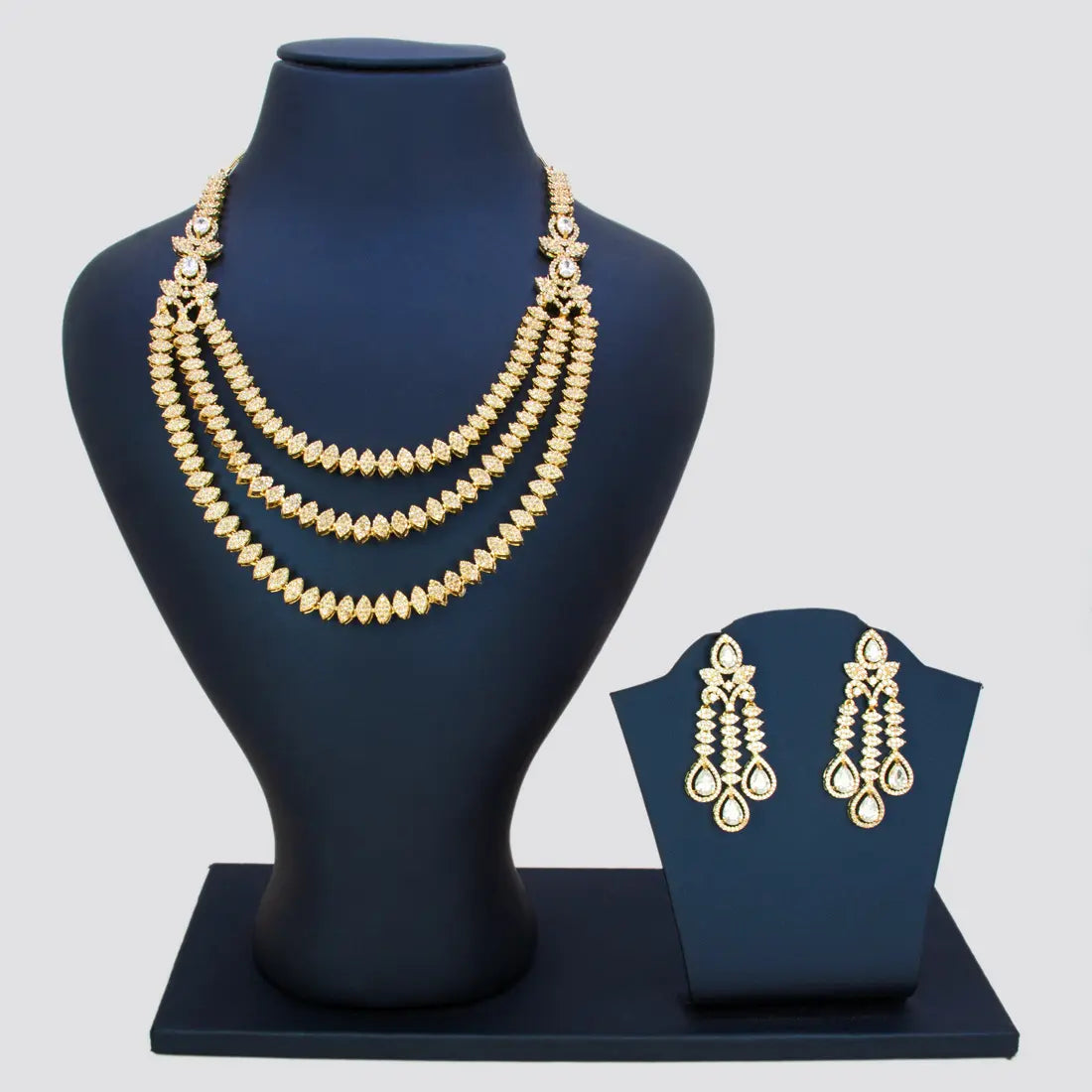 Gold pated CZ necklace and earrings on black mannequin and display stand against a gray background