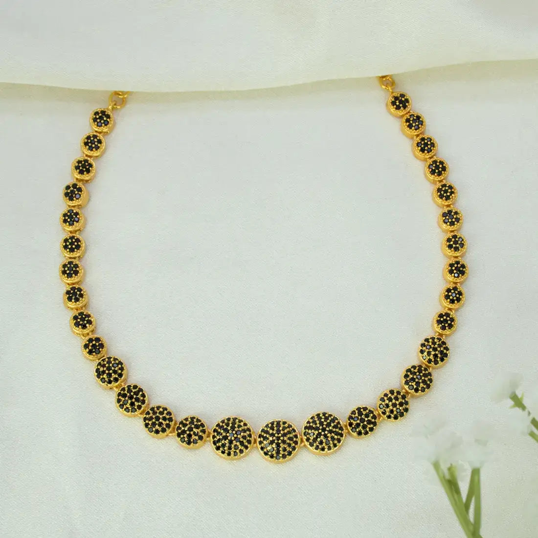 A Gold-Plated Round Design Stone Necklace featuring circular disc charms paved with small black CZ stones on a soft white fabric background.