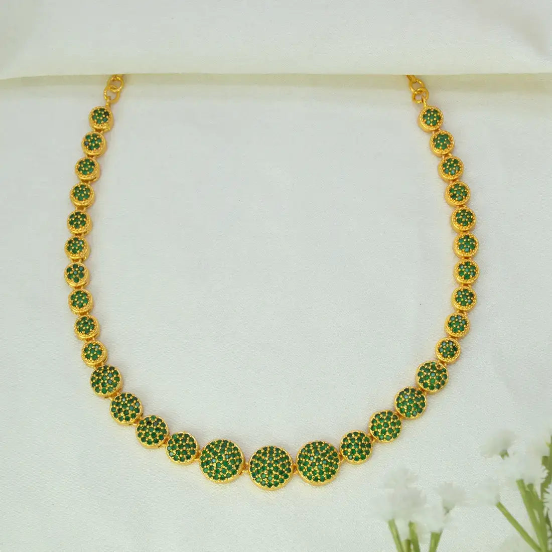 A Gold-Plated Round Design Stone Necklace featuring a series of round bezel-set green emeralds has clusters, displayed on a soft white fabric background.