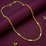 A gold chain necklace with rectangular bar links, draped elegantly over a deep purple rolled fabric backdrop with small white flower accents.