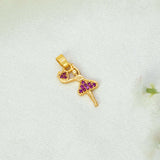 A gold-plated ballerina dancer pendant  with a ruby stone heart and purple diamond-patterned dress, resting on a textured white fabric background.
