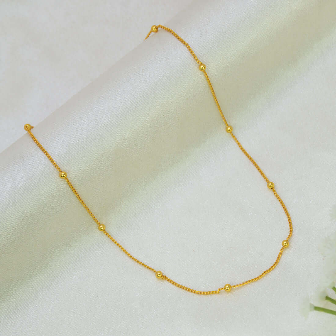 Gold-Plated Beaded Curb Link Baby Chain necklace with evenly spaced small gold beads, displayed on a soft, light-colored fabric background.