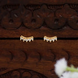 A pair of Gold-Plated Cubic Zirconia Arc Second Stud Earrings with small clear stones, displayed on a dark carved wooden surface.