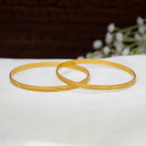 Gold-Plated Designer Cutting Bangles with engraved wave patterns, resting on a white textured surface with a blurred dark brown background and white flowers.