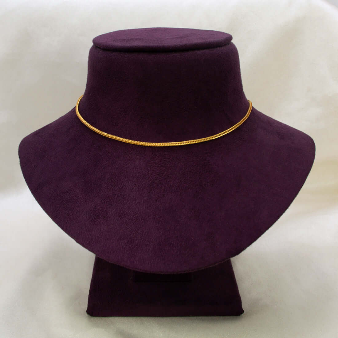 A Gold-Plated Foxtail Chain for babies is displayed on a dark purple velvet jewelry bust against a light beige fabric background.