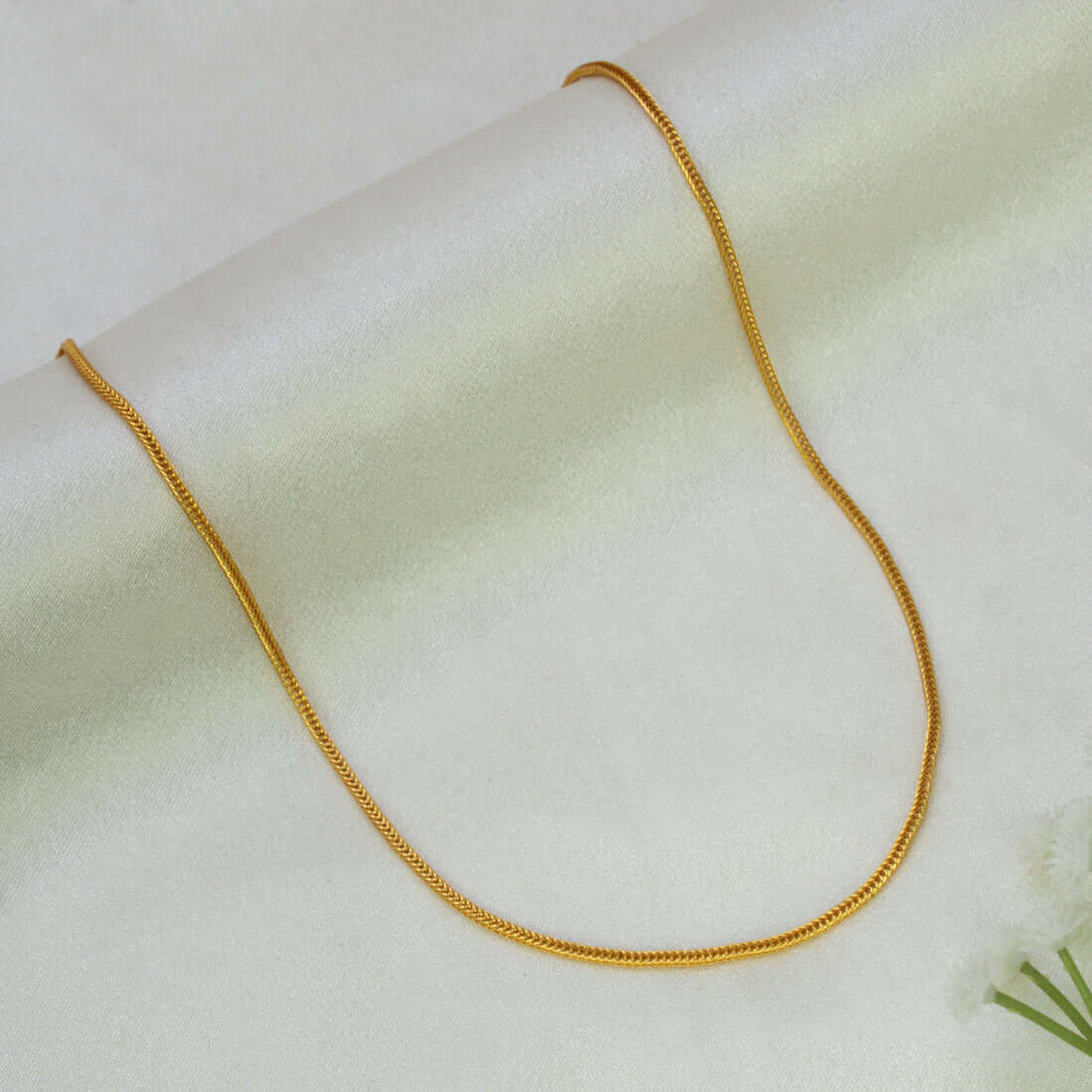 A Gold-Plated Foxtail Chain for Babies necklace draped in a U-shape over a soft, light cream-colored fabric background.