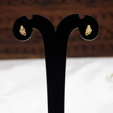 A pair of Gold-Plated Leaf Design CZ Stone Second Studs displayed on a black T-shaped jewellery stand against a blurred brown and white background.