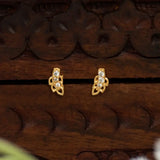 A pair of Gold-Plated Leaf Design CZ Stone Second Studs with clear cubic zirconia stones, displayed on a dark brown carved wooden surface.