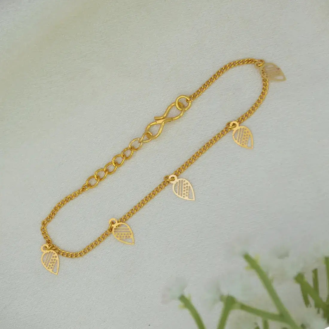 A delicate Gold-Plated Leaf Hanging Bracelet with three small leaf-shaped charms, displayed on a soft, light-colored textured surface.