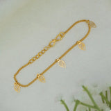 A delicate Gold-Plated Leaf Hanging Bracelet with three small leaf-shaped charms, displayed on a soft, light-colored textured surface.