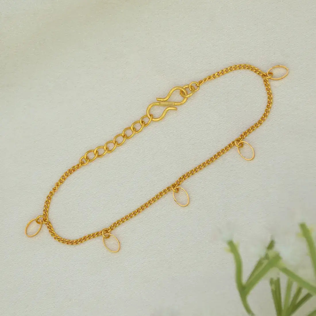 A delicate Gold-Plated Oval Hanging Chain Bracelet with three small oval dangling charms, laid flat on a light textured background.