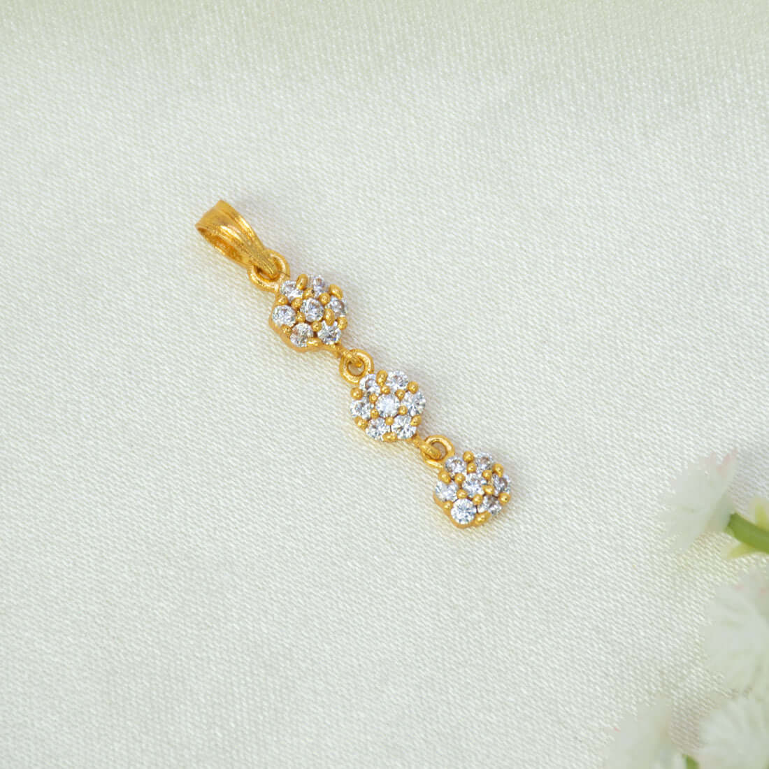 A gold-plated three-tier stone floral drop pendant charm featuring three small floral clusters of CZ stones, displayed on a textured off-white fabric background.