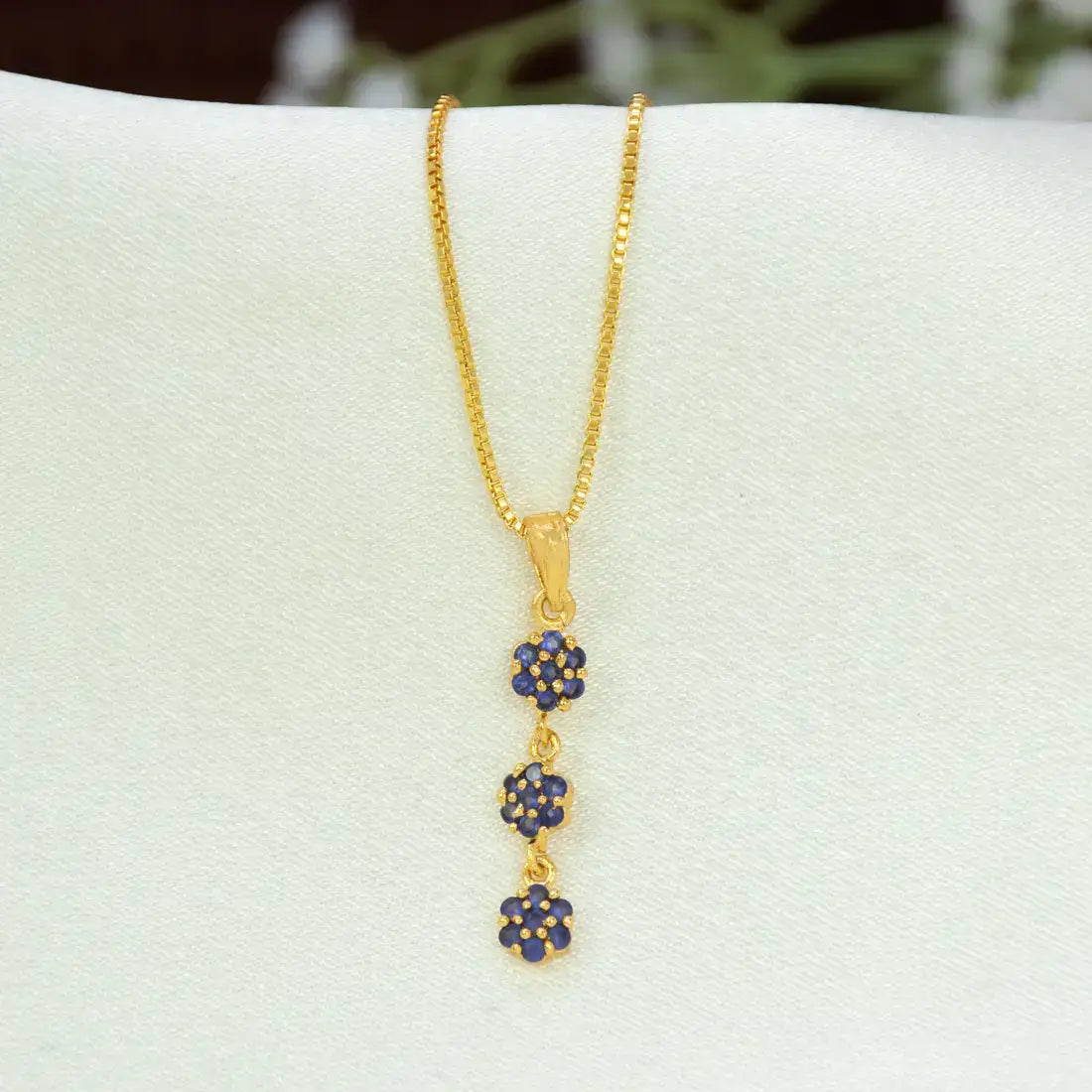 A gold chain necklace with a vertical dangle Gold-Plated Three-tier Stone Floral Drop Pendant featuring three small flower clusters, each set with deep blue stones, displayed on a white jewelry bust.