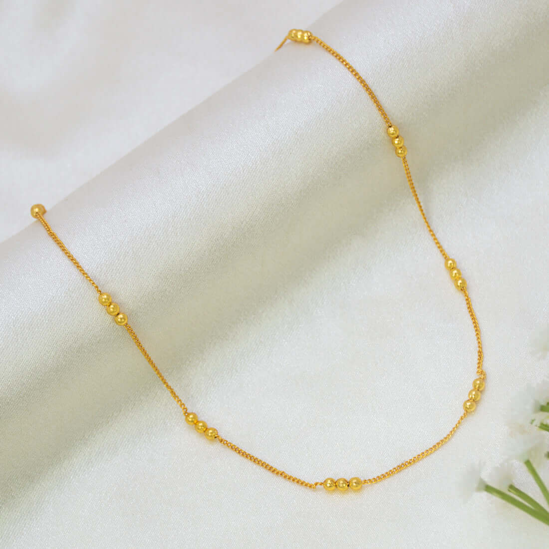 A delicate Gold-Plated Triple-Beaded Curb Chain for Kids with small, evenly spaced round gold beads, displayed on a soft, draped white satin fabric.