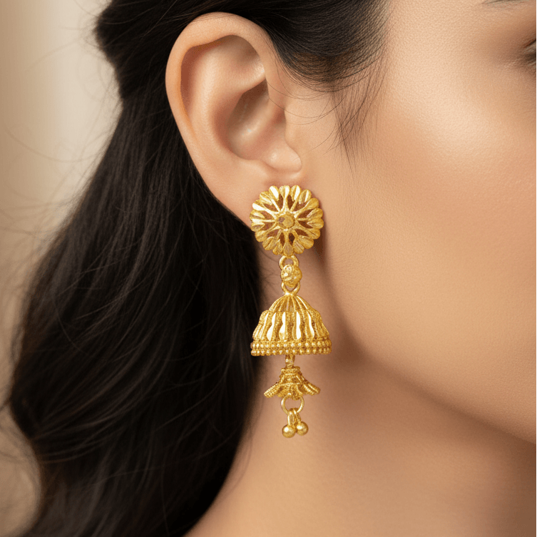 A close-up of a woman's ear wearing a detailed Gold-Plated Two-Step Floral Jhumka Earrings with a floral top, bell-shaped dangle, and small hanging bells.