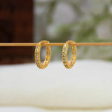 A pair of Gold-Plated CZ Hoop Earrings  with small clear stones set along the front, hanging from a thin wooden rod against a softly blurred light background.