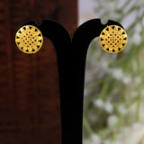 A pair of Gold Plated Sunflower Stud Earrings For Women with intricate geometric cutout patterns, displayed on a black stand against a blurred brown and white background.