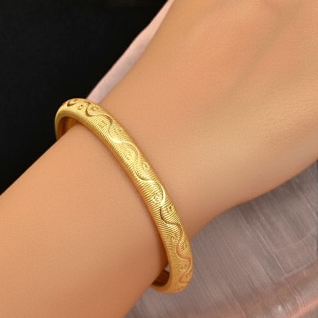 a gold-plated bangle bracelet with an intricate wave pattern design. 