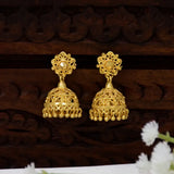 A pair of ornate Grand Traditional Gold-Plated Filigree Jhumka Earrings displayed against a dark carved wooden background with small white flowers in the foreground.