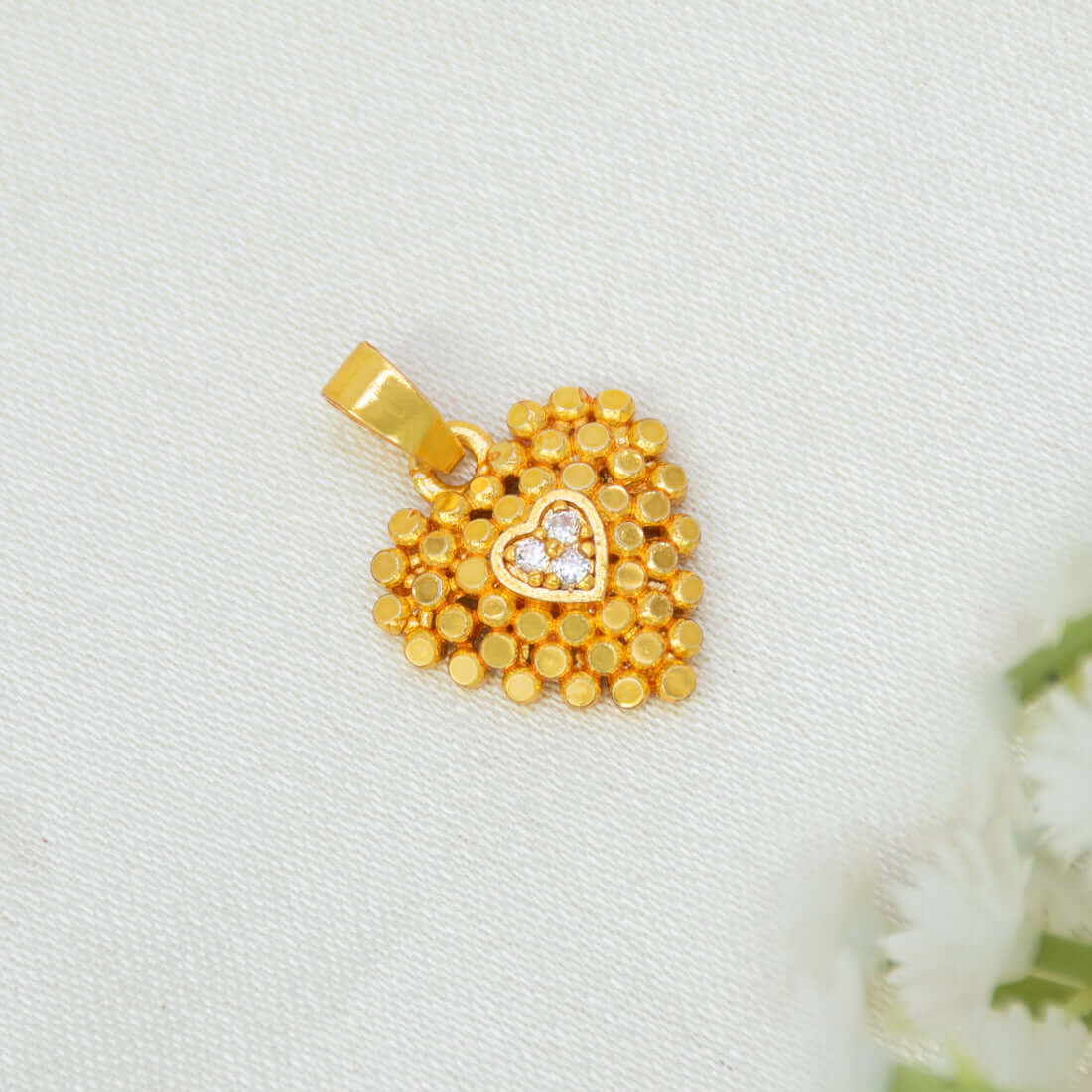 A Heart-Shaped Gold-Plated CZ Pendant For Women with a textured beaded border and a small central heart set with a clear stone, displayed on a textured white fabric background.