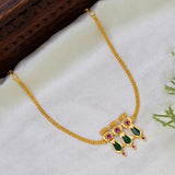 Kerala Gold-Plated Triple Nagapadam Necklace with a decorative pendant featuring green Nagapadam-shaped stones and small synthetic ruby stones, displayed on a white fabric surface with a dark wooden prop.