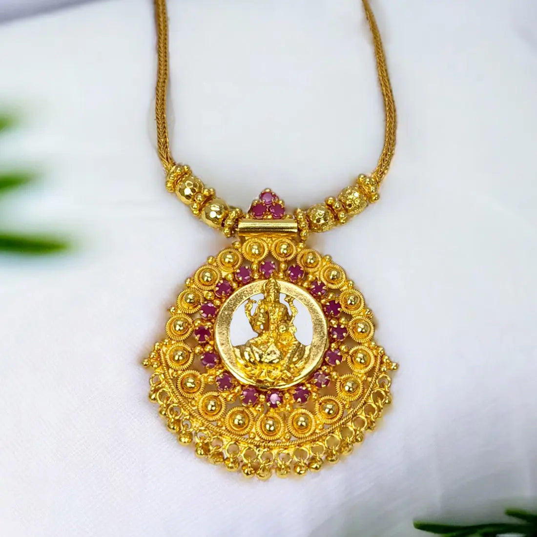 Ethnic Gold Plated Ruby Stones Lakshmi Pendant Necklace decorated with ruby stones and intricate gold bead detailing.