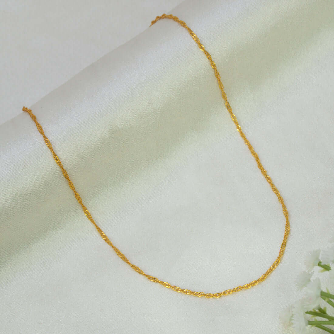 A delicate Popular Gold-Plated Twisted Singapore Chain draped in a U-shape on a soft, off-white textured fabric background.