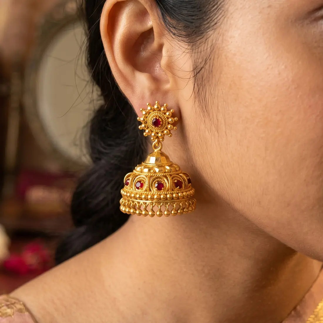 Red Stone Gold Plated Big Jhumka Earrings displayed on model, showcasing intricate design and craftsmanship.