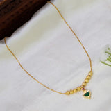 A gold-plated chain necklace with a textured bead bar and a small Palakka-shaped pendant featuring a green center and a pink ruby stone, displayed on a white fabric background.
