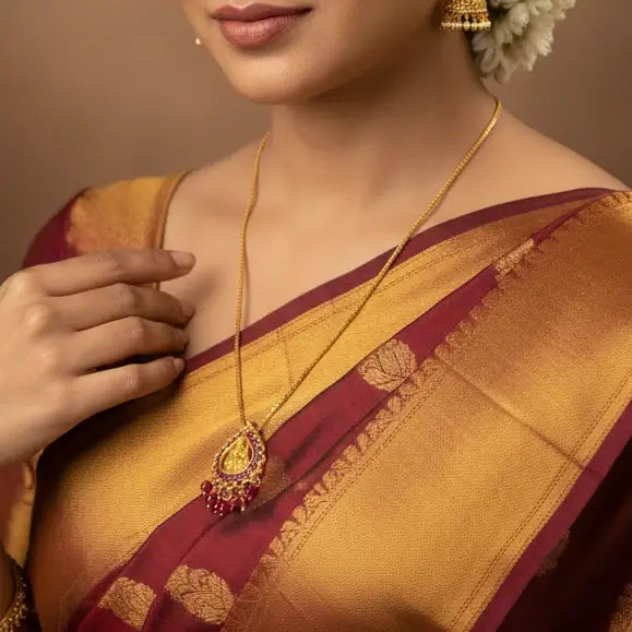 A gold chain necklace with a decorative pendant featuring a gold-toned central Lakshmi motif and ruby stones, displayed on a soft white fabric surface.
