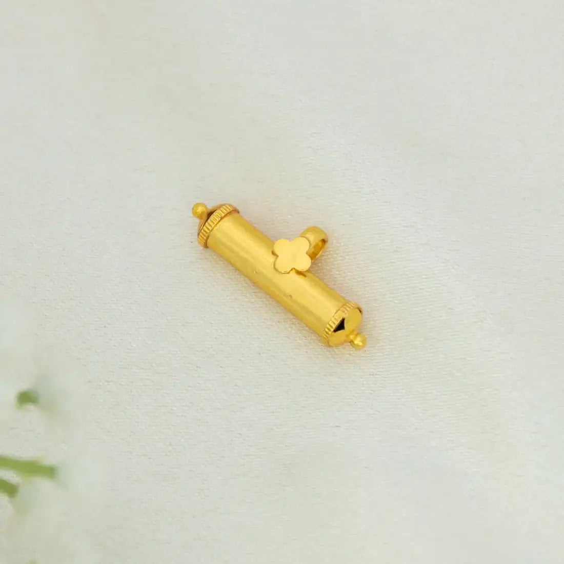 Small Gold Plated Cylindrical Amulet/Elasu Pendant with a clover-shaped detail, photographed on a light cream fabric background.