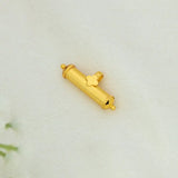 Small Gold Plated Cylindrical Amulet/Elasu Pendant with a clover-shaped detail, photographed on a light cream fabric background.