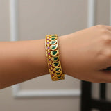 South Indian One Gram Gold Broad Mango Bangle with green and ruby accents worn on model's wrist.
