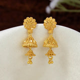 A pair of ornate South Indian Gold-Plated Floral Stud Two-Step Jhumkas displayed on a white fabric stand against a dark brown blurred background.