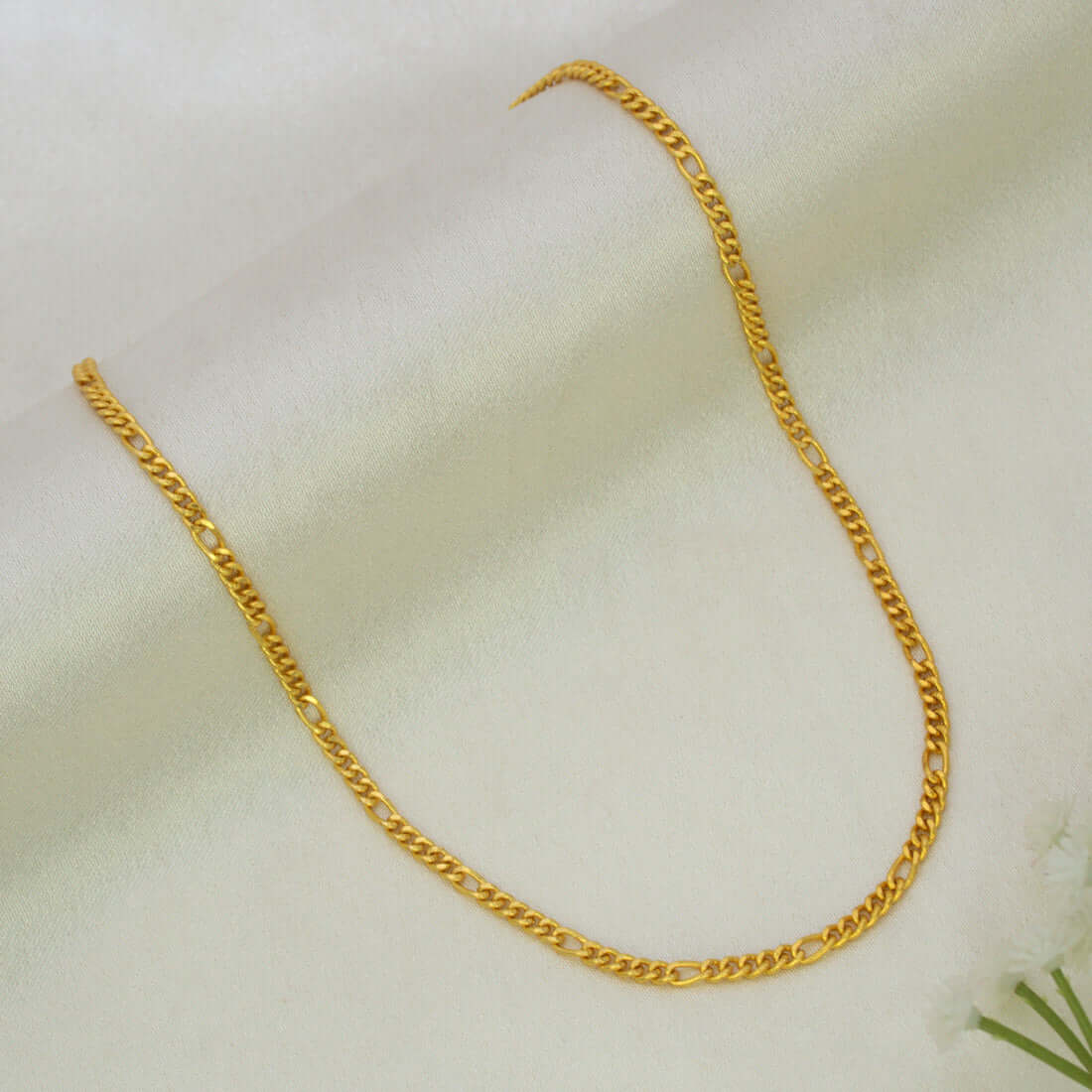 A Unisex Gold Plated Figaro Sachin Chain arranged in a U-shape on a soft, off-white textured fabric background.