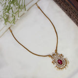 Victorian Antique Gold Peacock Stone Pendant Necklace with an ornate pendant featuring a central oval red gemstone and surrounding clear stones, displayed on a white fabric surface with small white flowers in the corner.