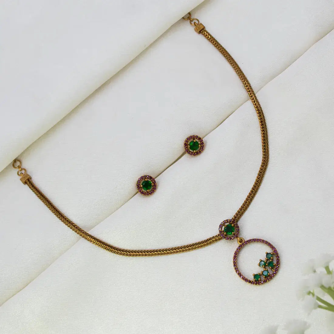 Victorian Gold-Plated Stone Necklace & Earring Set with ruby emerald stone accents, displayed on a white textured fabric background.