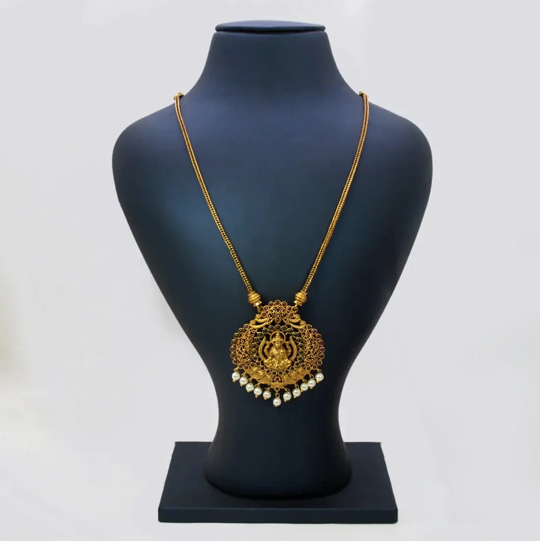 A pair of Victorian Style Lakshmi Kemp Stone Pendant Chain displayed on a black Y-shaped jewelry stand against a softly blurred indoor background with brown and white tones.