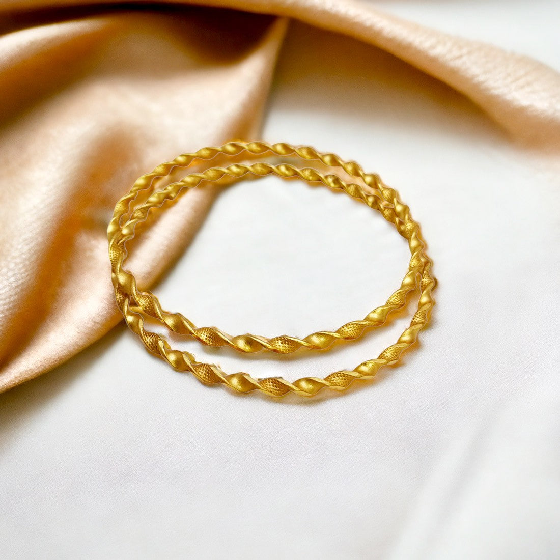 Elegant Gold Plated Twisted Spiral Bangles showcased on a soft fabric background.