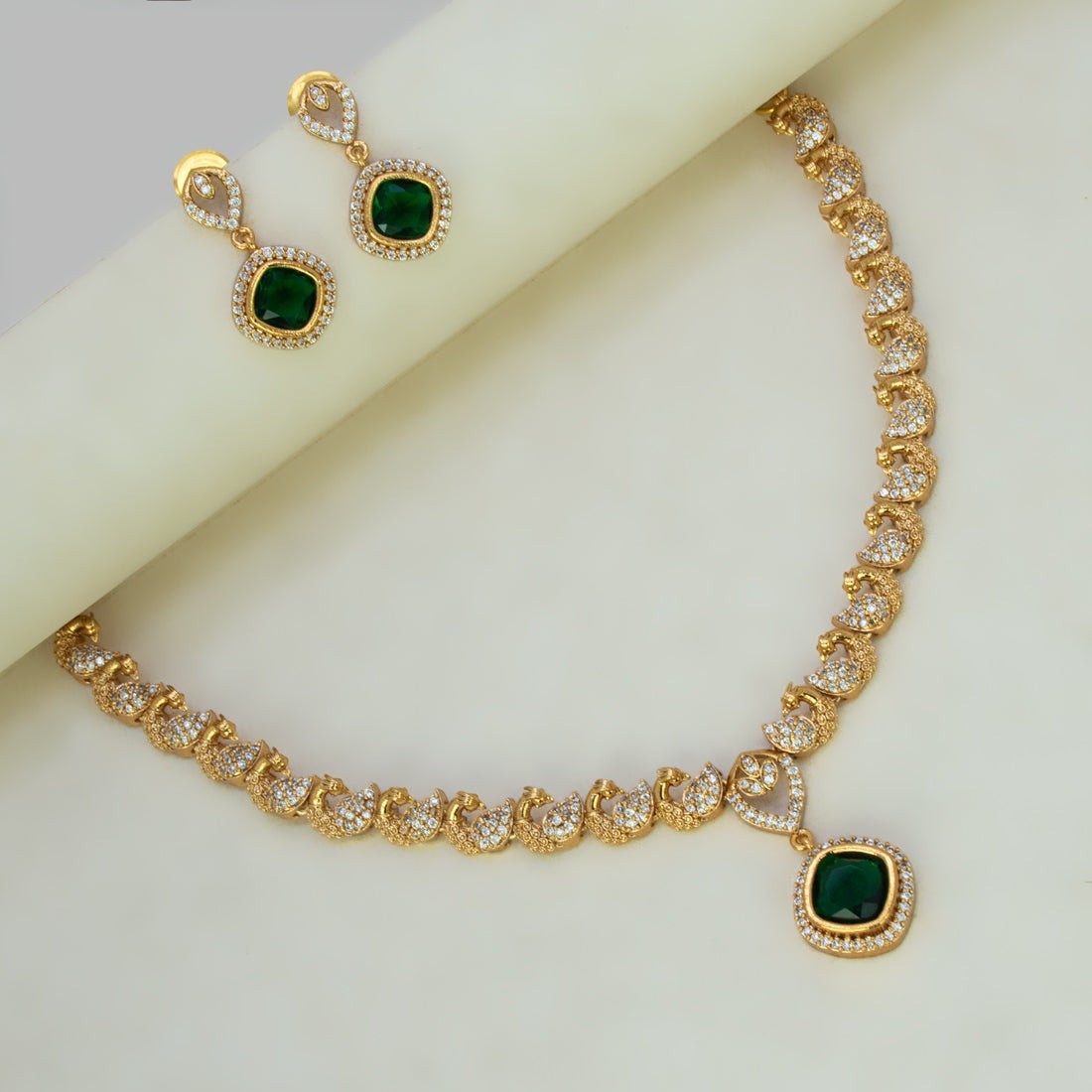 K Supreme gold-plated necklace set with peacock motifs and emerald green cubic zirconia stones, includes matching earrings.