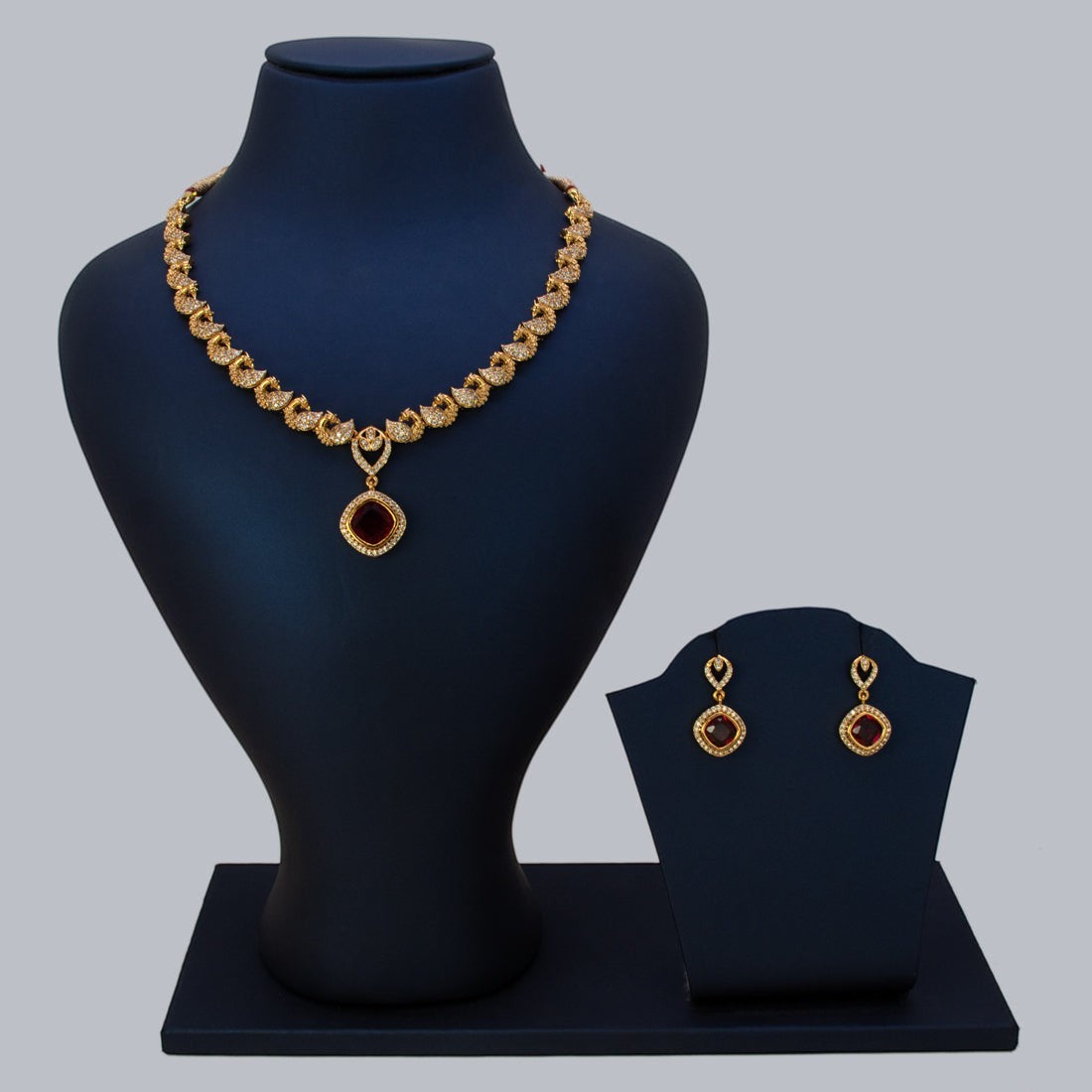 K Supreme gold-plated necklace set with peacock motifs and a ruby red cubic zirconia pendant and matching earrings.