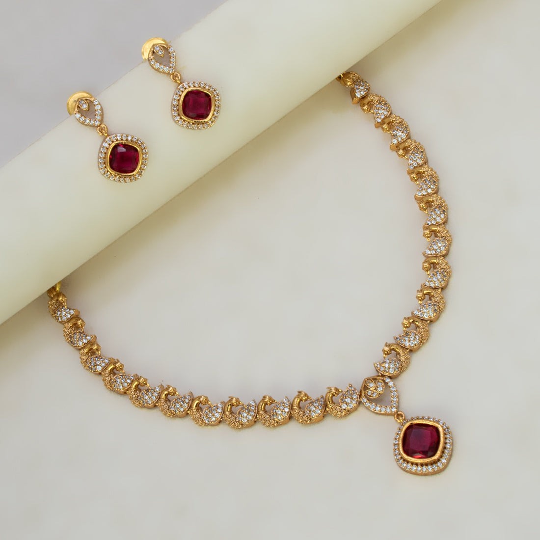 K Supreme gold-plated necklace set with ruby red cubic zirconia stones in a peacock design, includes matching earrings.